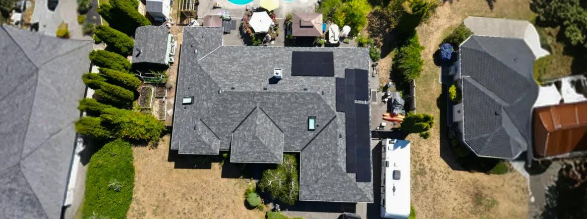 Top-down view of a professional solar panel array on a grey shingle residential roof, showcasing a sleek and efficient layout in a BC neighborhood.