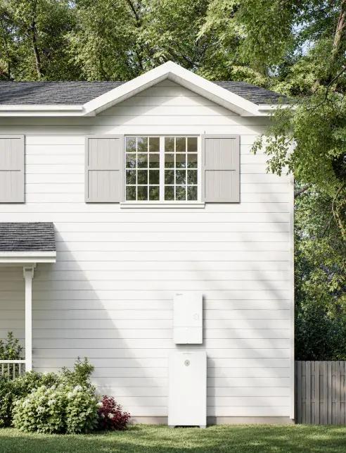 Weather-resistant outdoor installation of a residential backup battery storage unit mounted on the exterior white siding of a home.