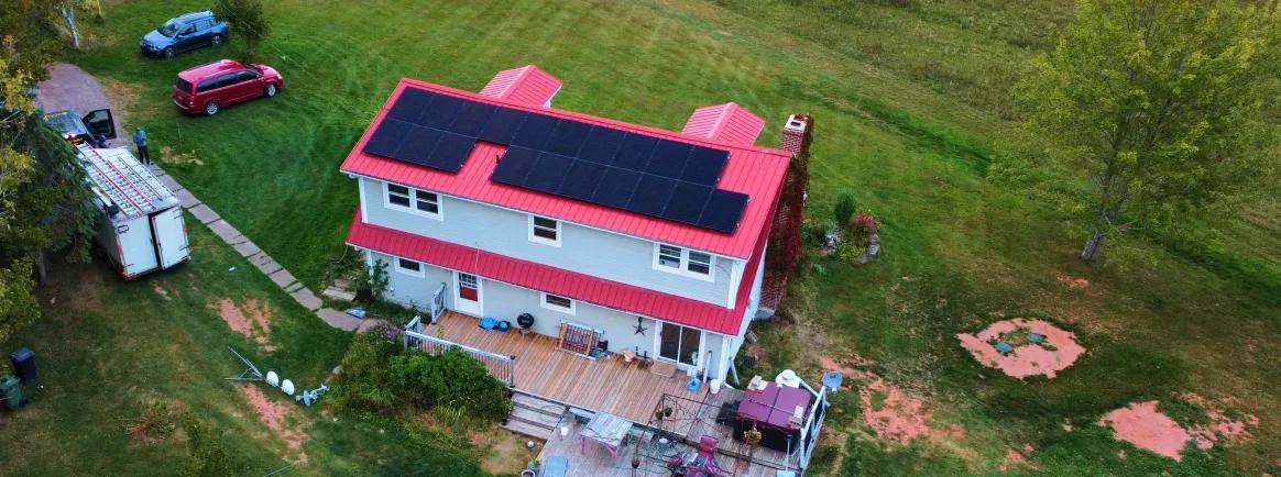 Side-view of a professional solar array on a red-roofed PEI home, showcasing sleek black panels and modern mounting hardware.