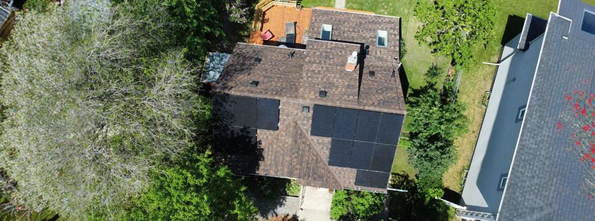 Close-up aerial shot of high-performance solar panels installed on a residential brown shingle roof in a suburban Alberta neighborhood.