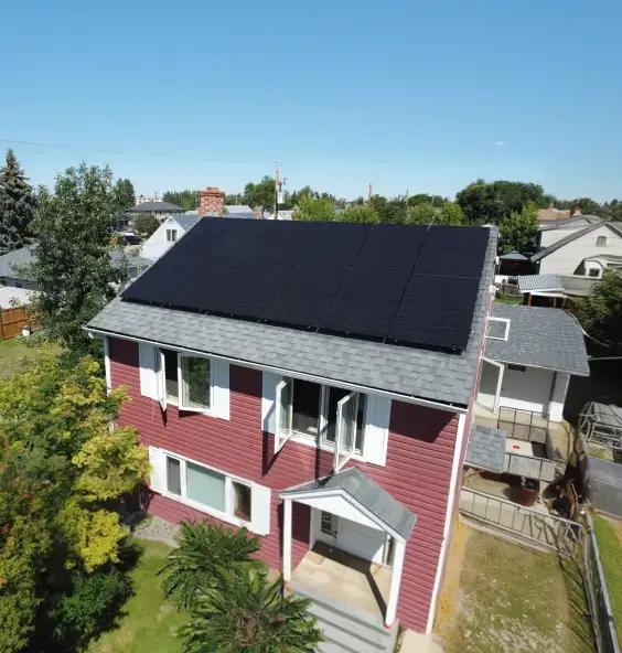 Side-angle view of a complete residential solar energy system on an Alberta home, showcasing sleek black panels under a clear, sunny sky.
