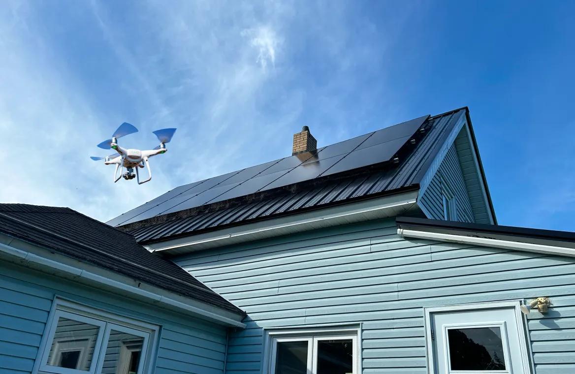 A drone flying above a house roof equipped with solar panels, capturing site assessment imagery.