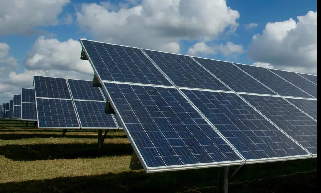 Row of ground-mounted solar panels in an open field.