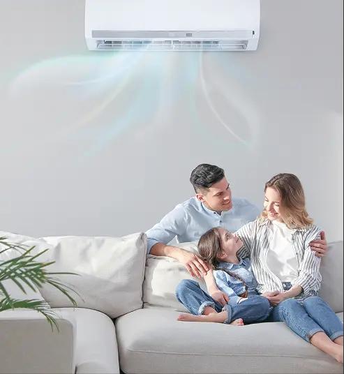 A happy family sitting together on a living room sofa beneath a wall-mounted ductless mini-split air conditioner blowing cool air.