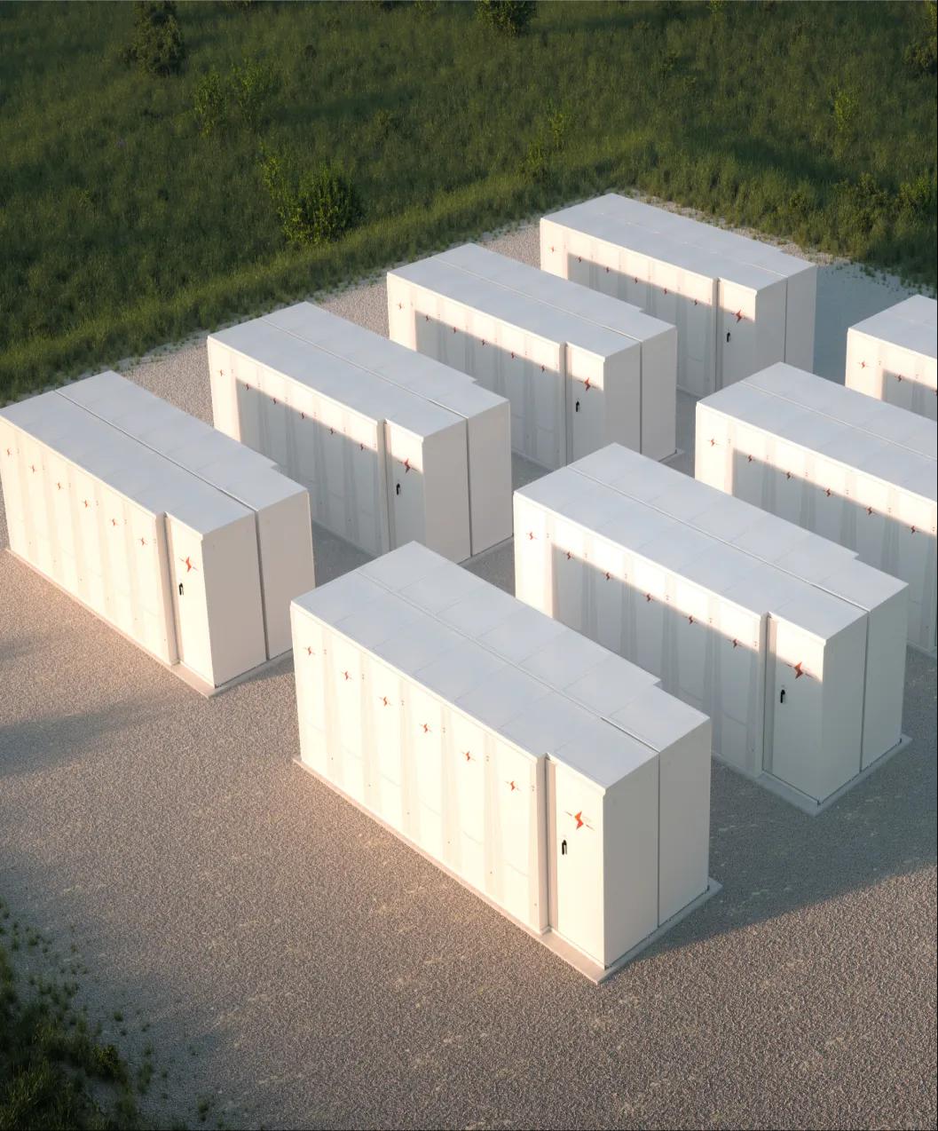 Aerial view of rows of white outdoor battery energy storage cabinets on a gravel pad.