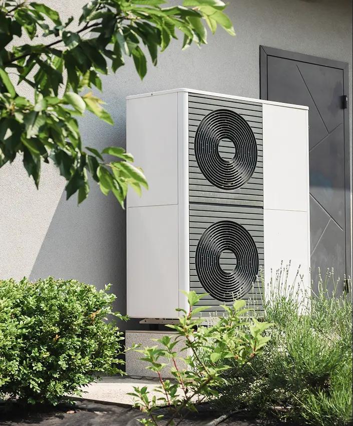 An energy-efficient white outdoor heat pump compressor unit with a dual-fan design installed outside a home.