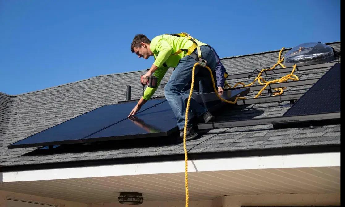 Installer fastening solar panels to a sloped shingle roof.